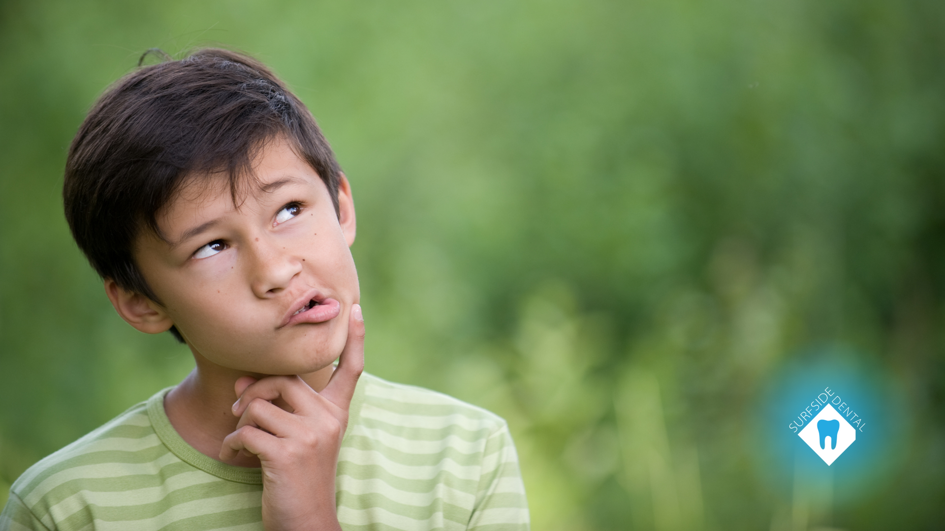 A young boy is holding his hand to his chin and looking up.