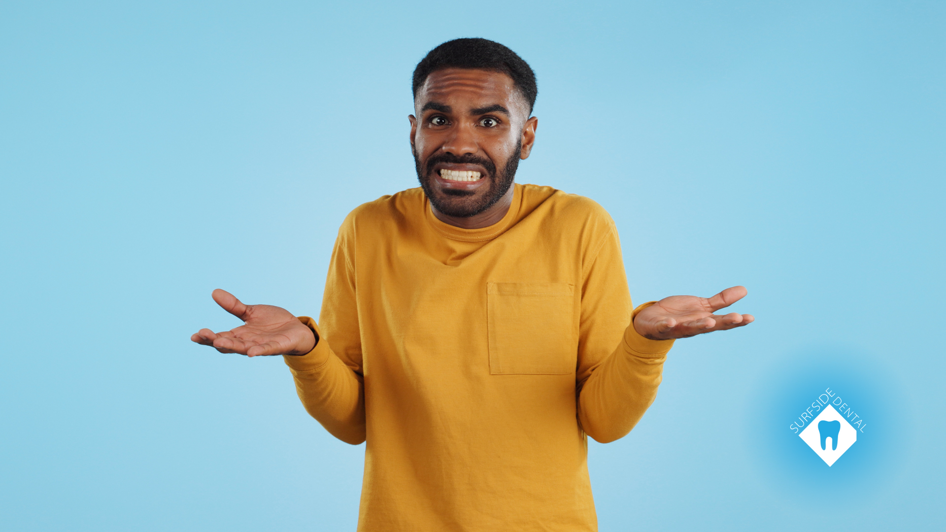 A man in a yellow sweater is shrugging his shoulders.