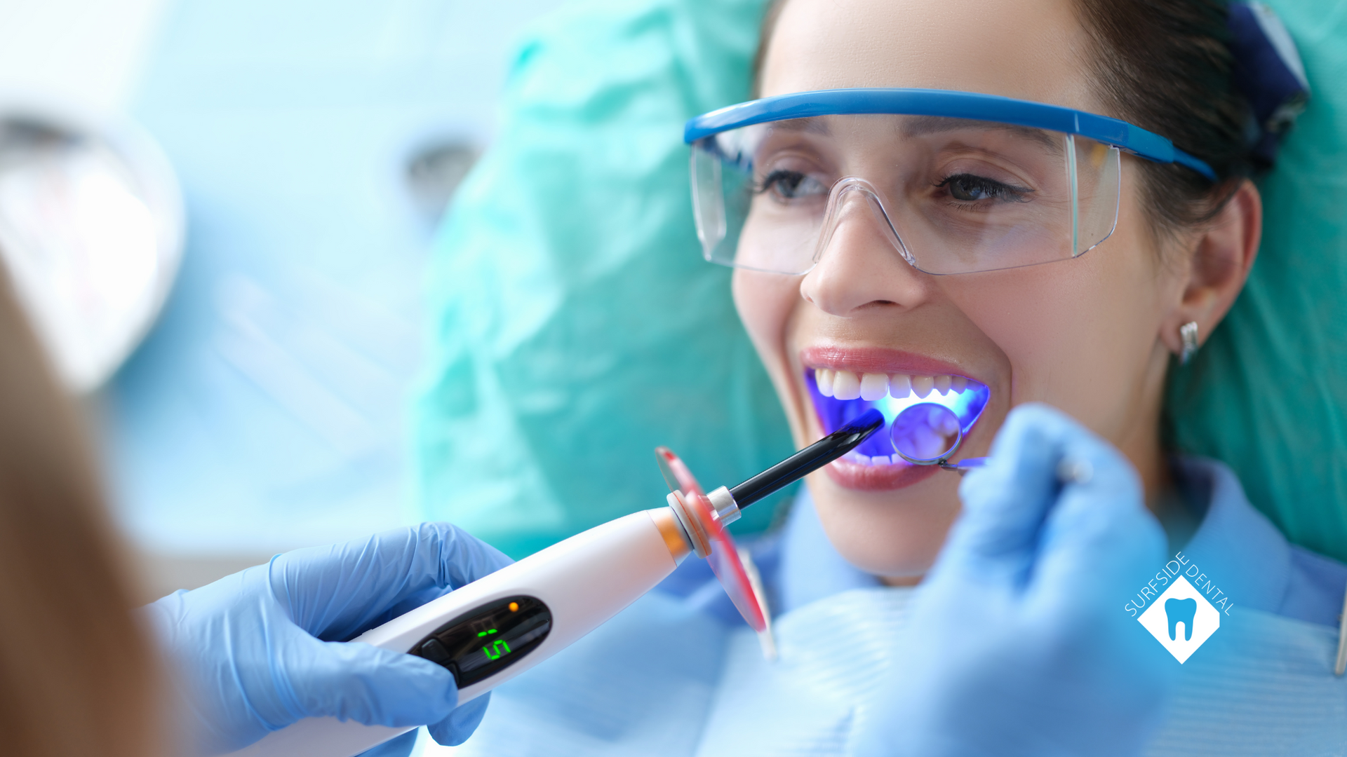 Woman at dentist receives light treatment, wearing protective eyewear, blue gloves, smiling.