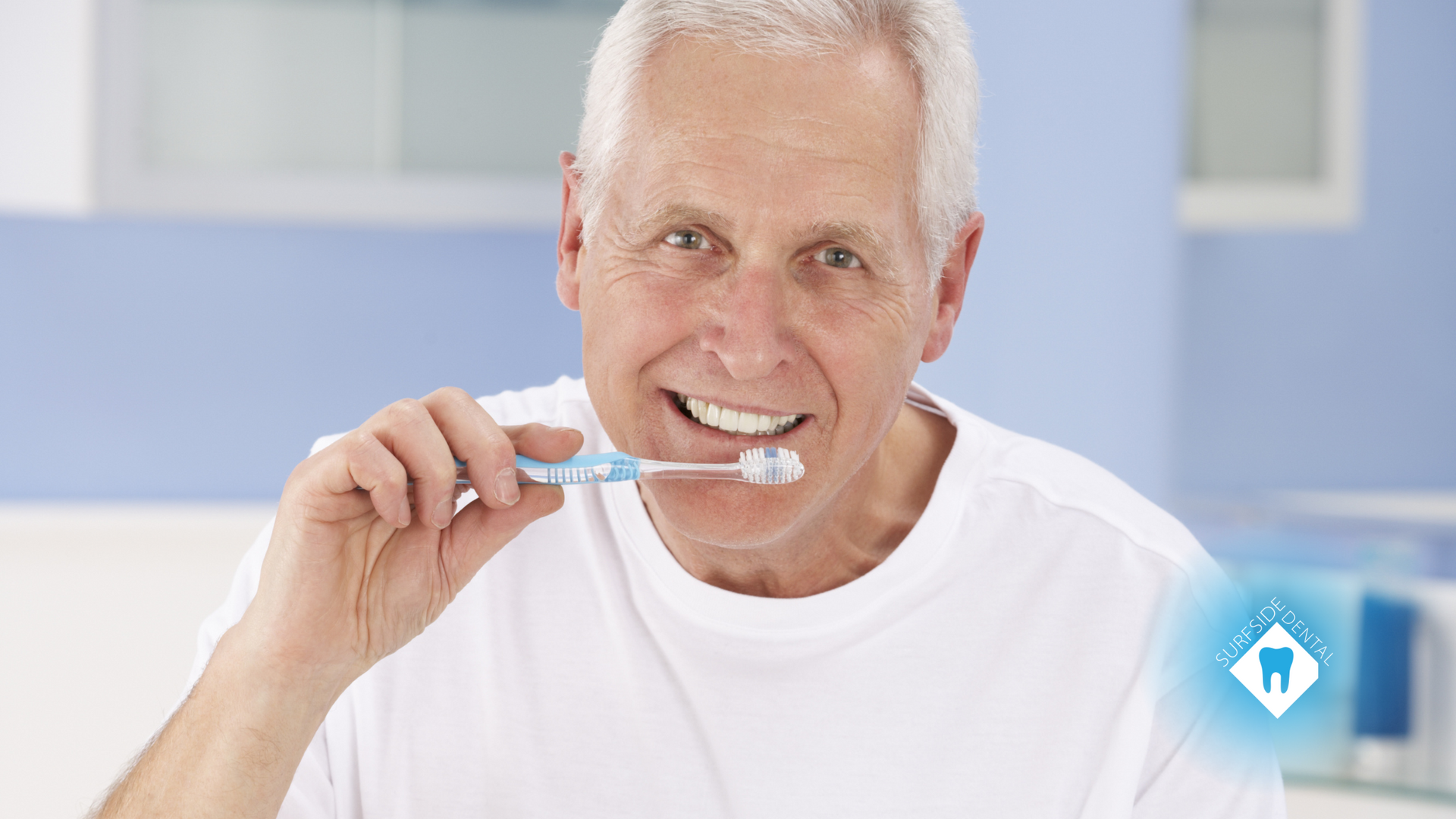 An elderly man is brushing his teeth in a bathroom.
