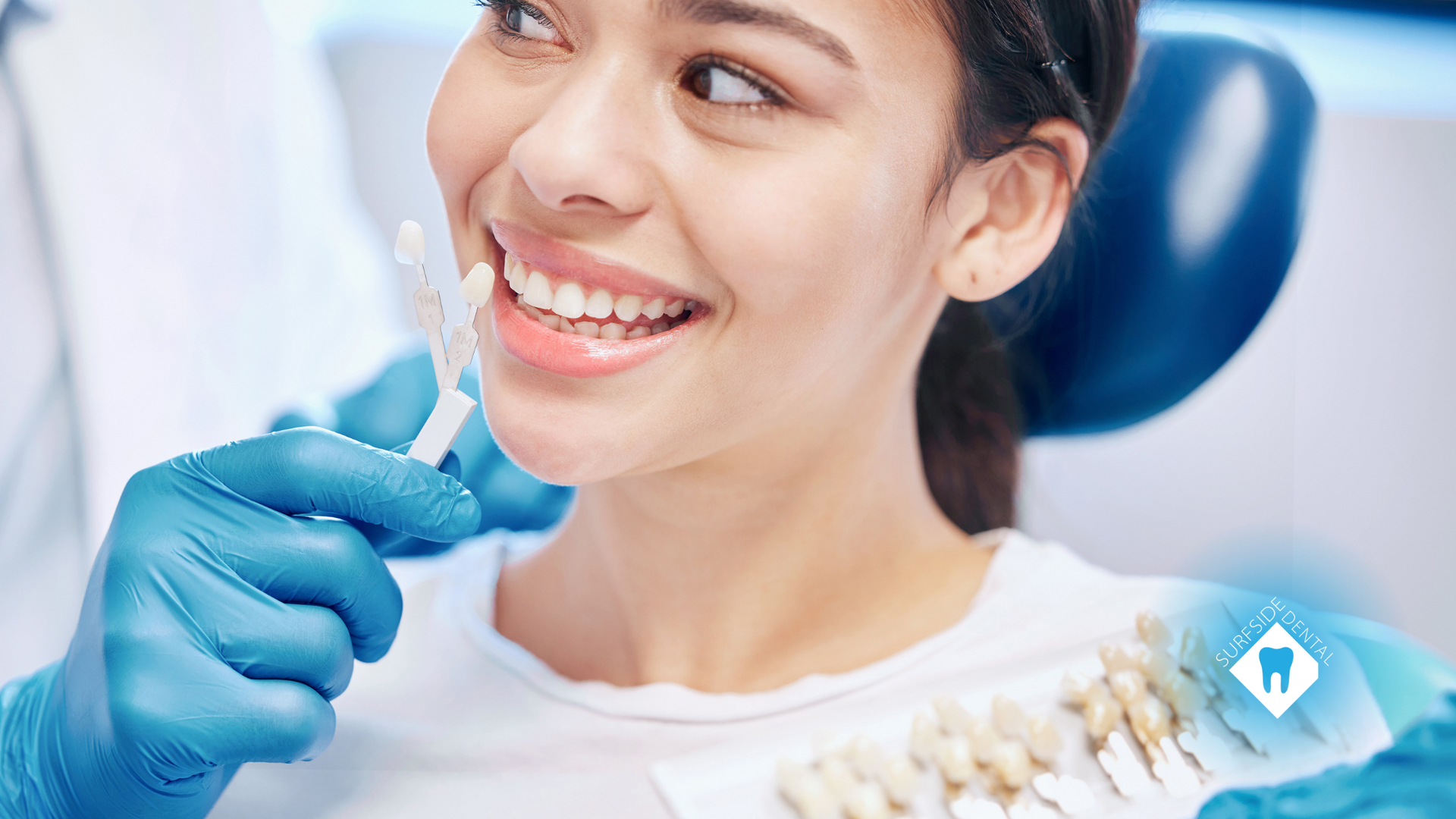 A woman is sitting in a dental chair holding a tooth color chart.