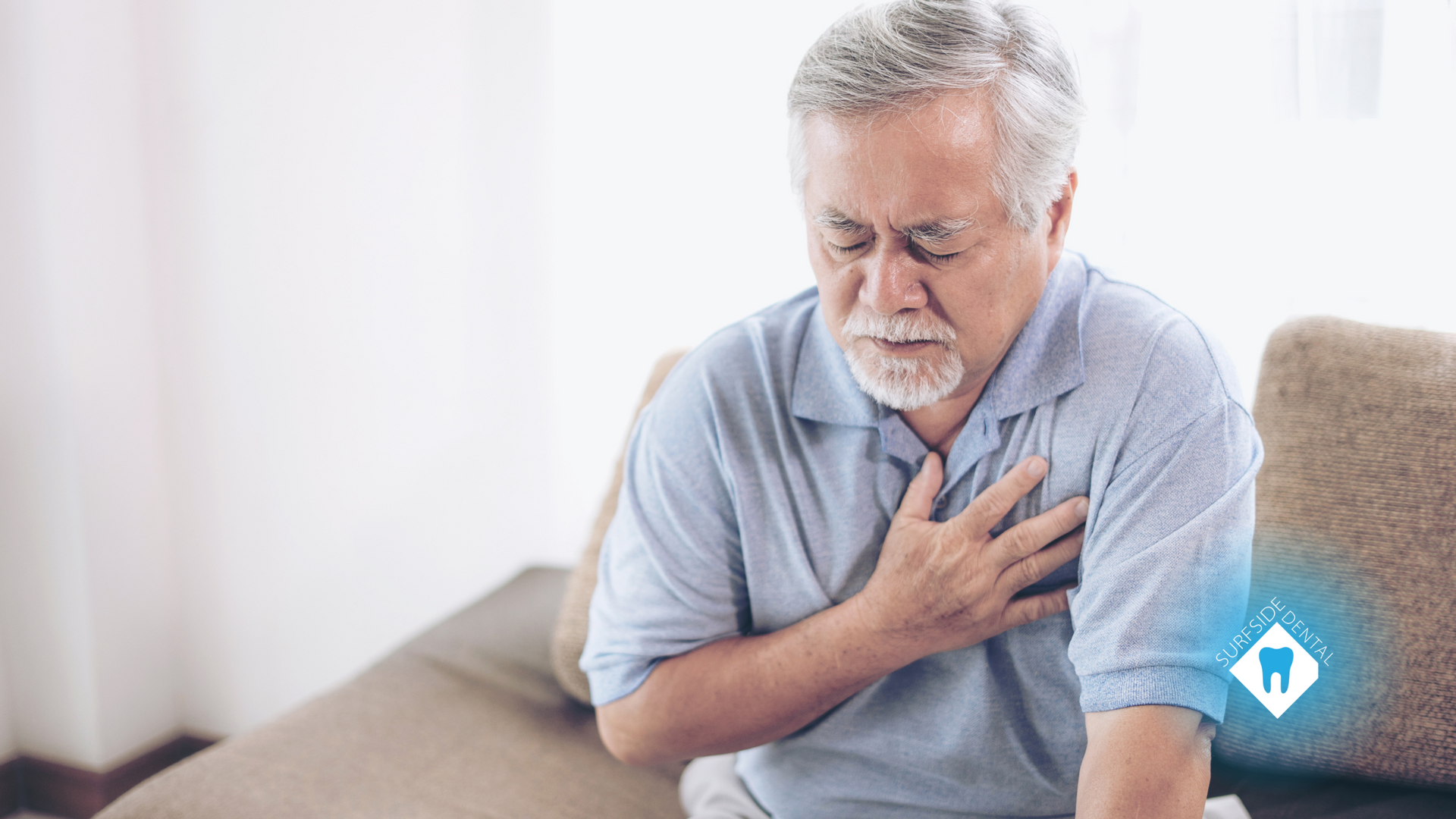 An older man is sitting on a couch holding his chest.