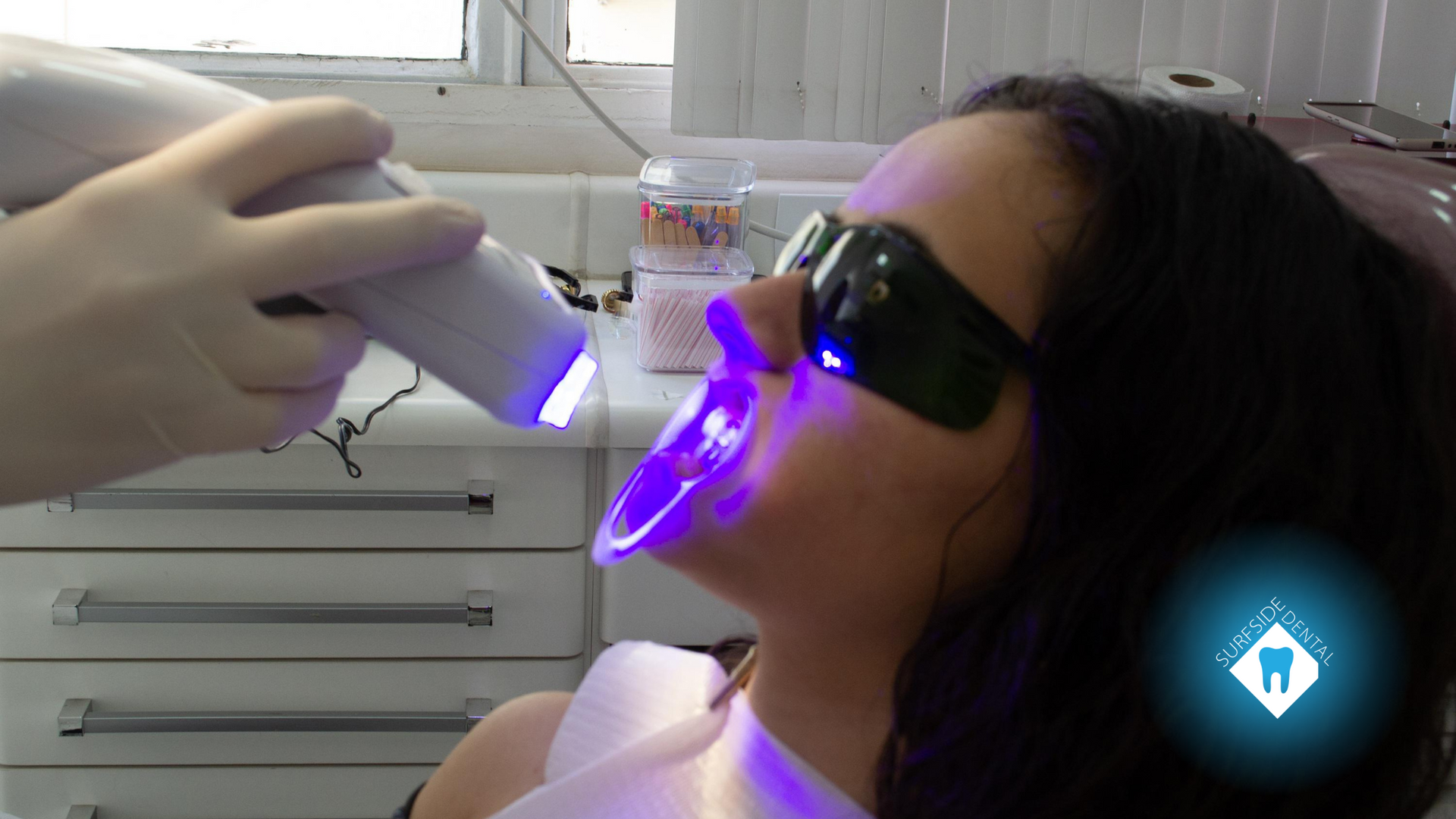 A woman is getting her teeth whitened in a dental office.