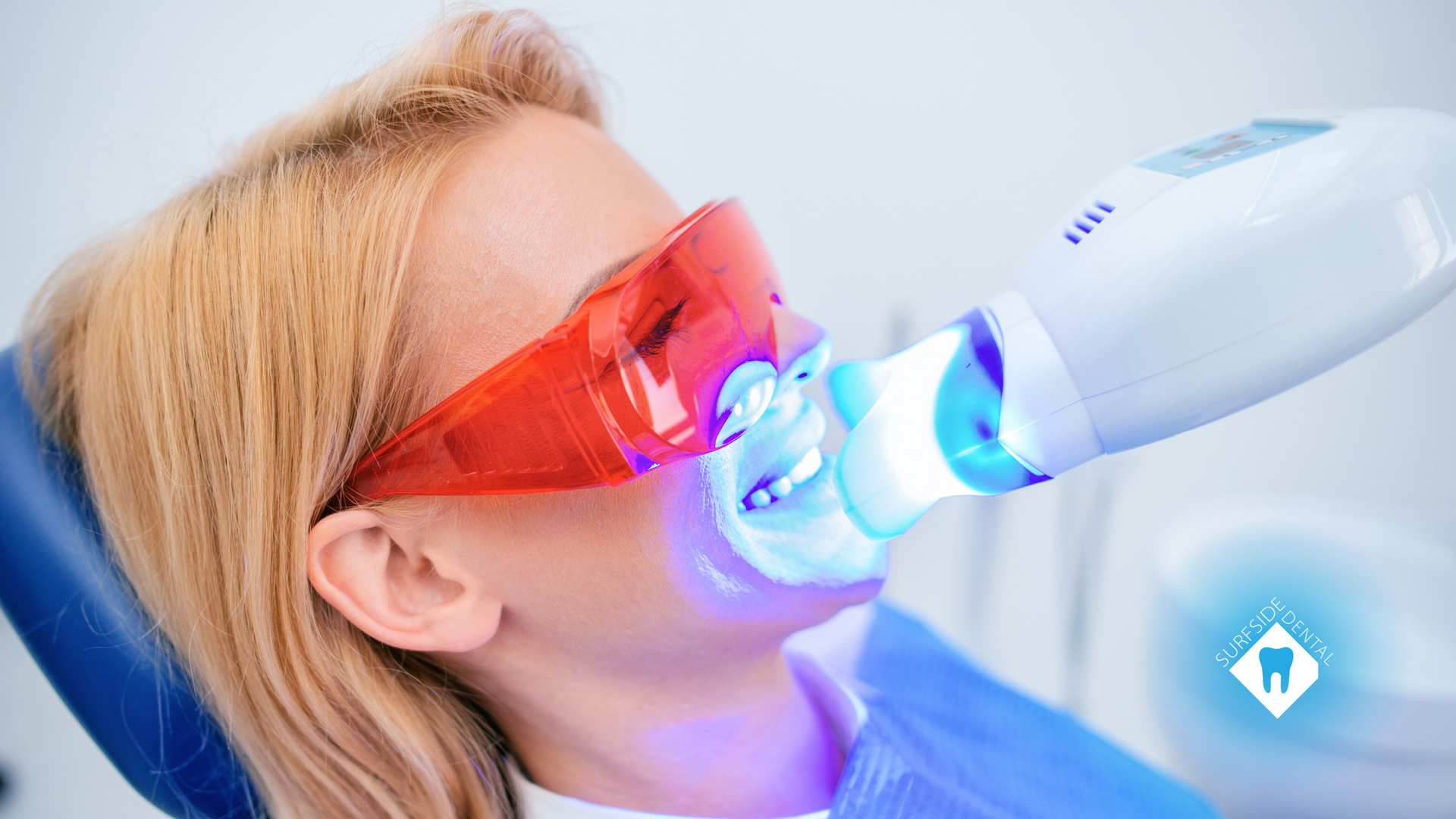 Woman undergoing professional teeth whitening with safety glasses on, in a dental chair.
