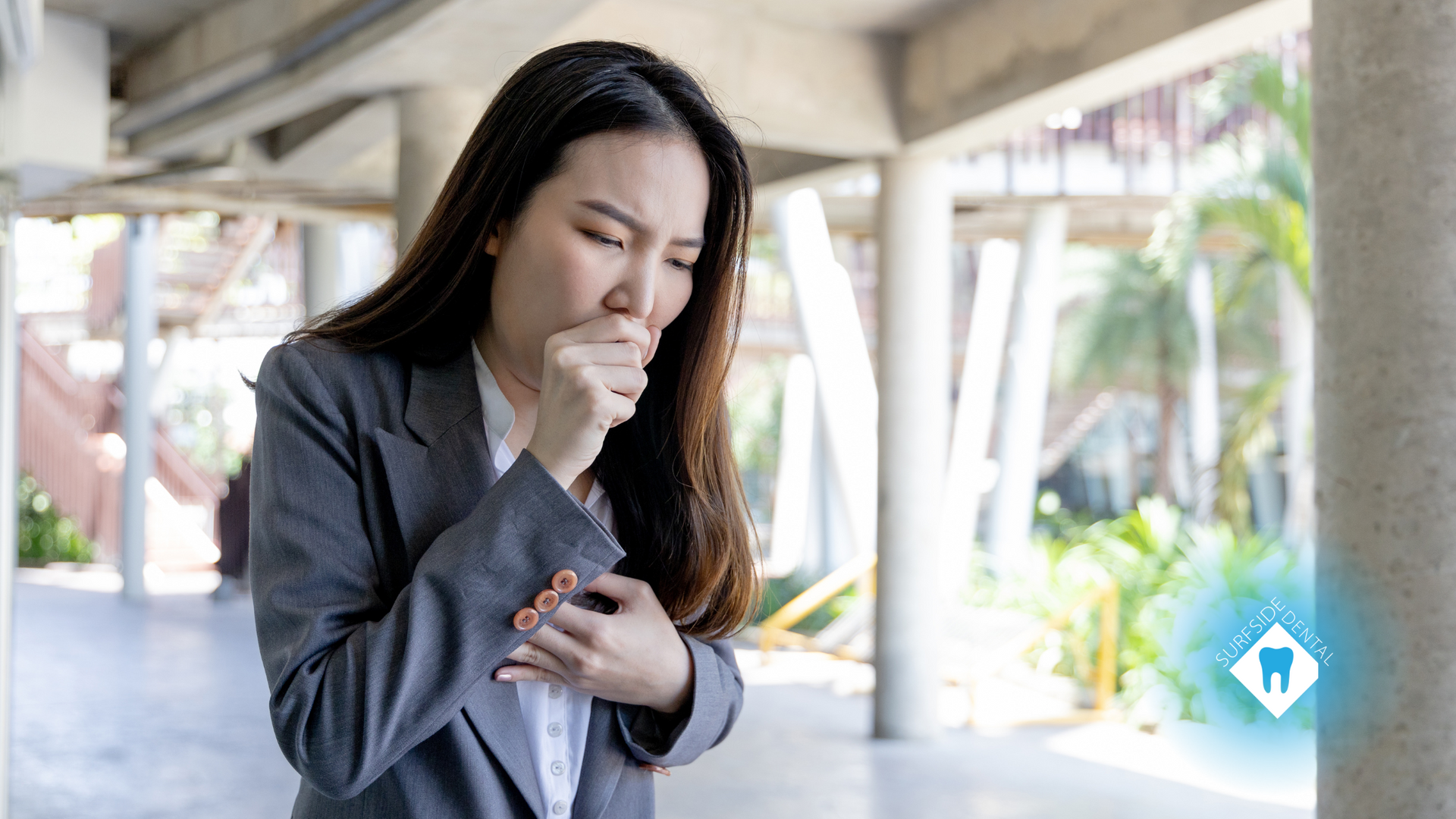 A woman in a suit is coughing while standing in a hallway.
