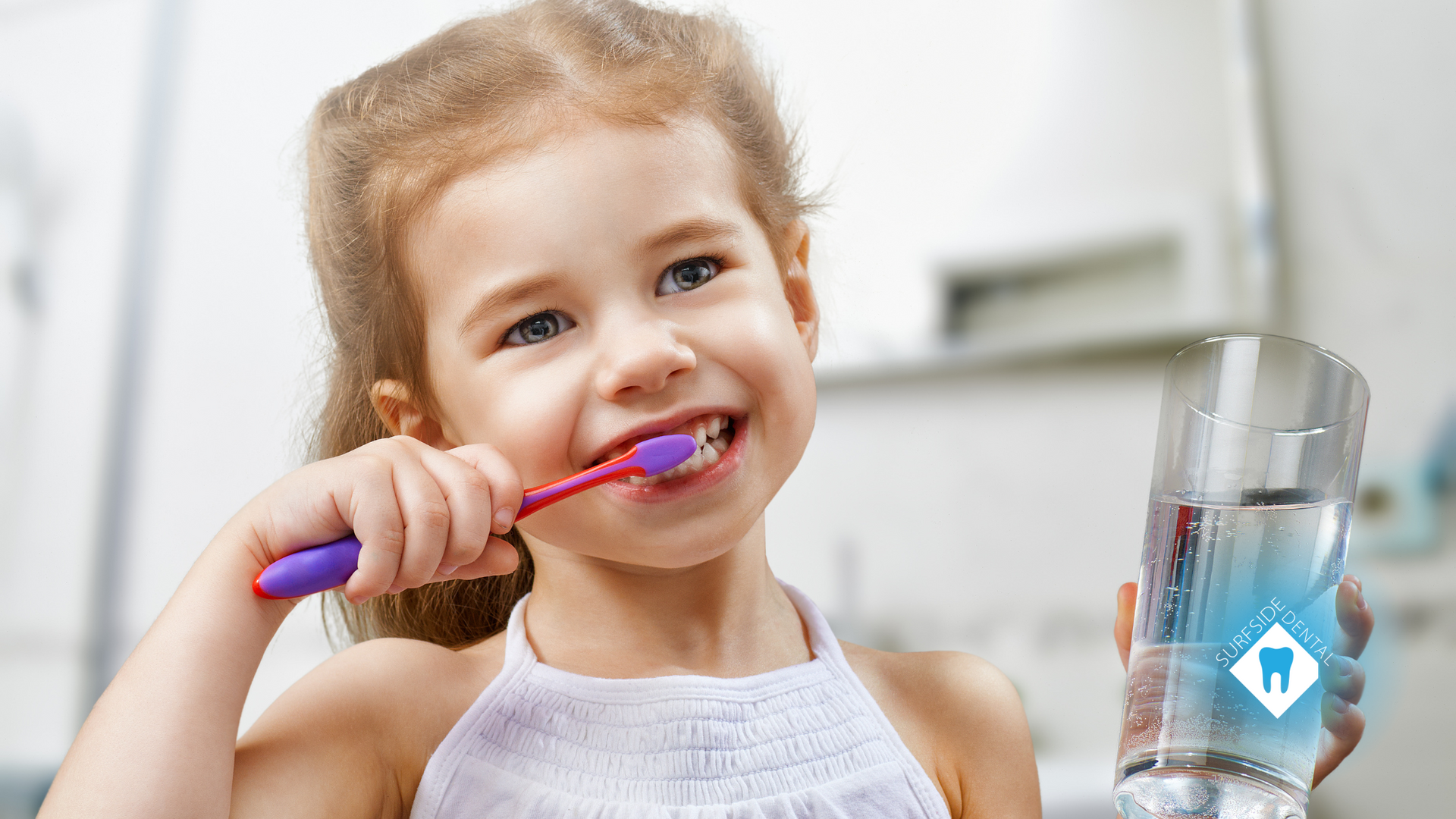 A little girl is brushing her teeth while holding a glass of water.