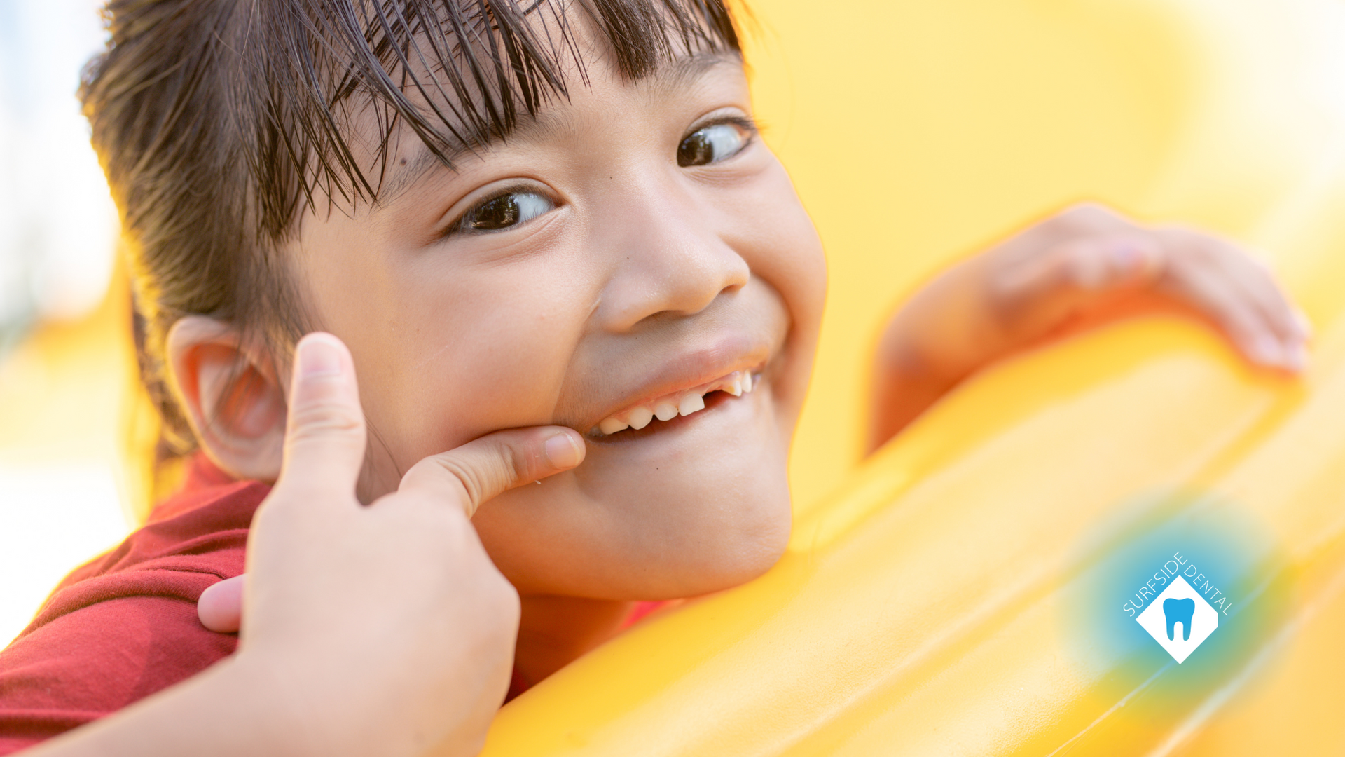 A little girl is giving a thumbs up while playing on a yellow slide.