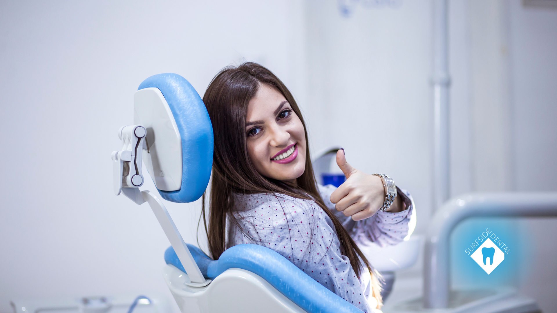 A woman is sitting in a dental chair and giving a thumbs up.