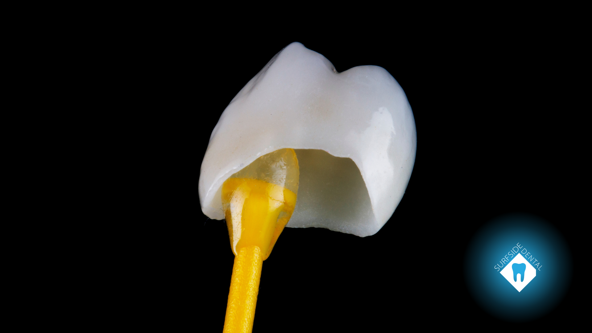 Dental crown being held with a yellow applicator against black background.