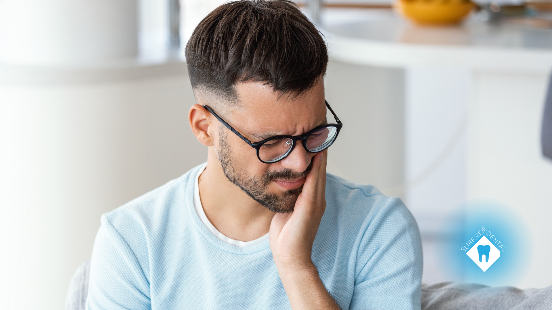 A man wearing glasses is holding his mouth in pain.