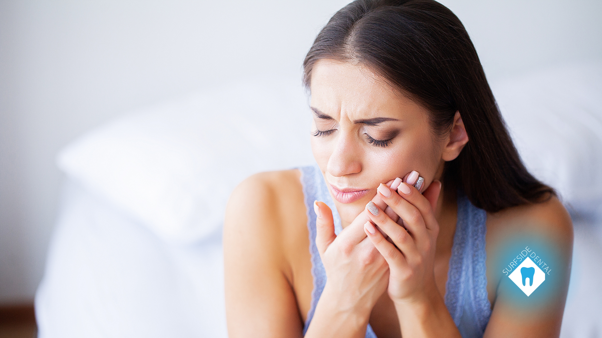 A woman is sitting on a bed with a toothache.