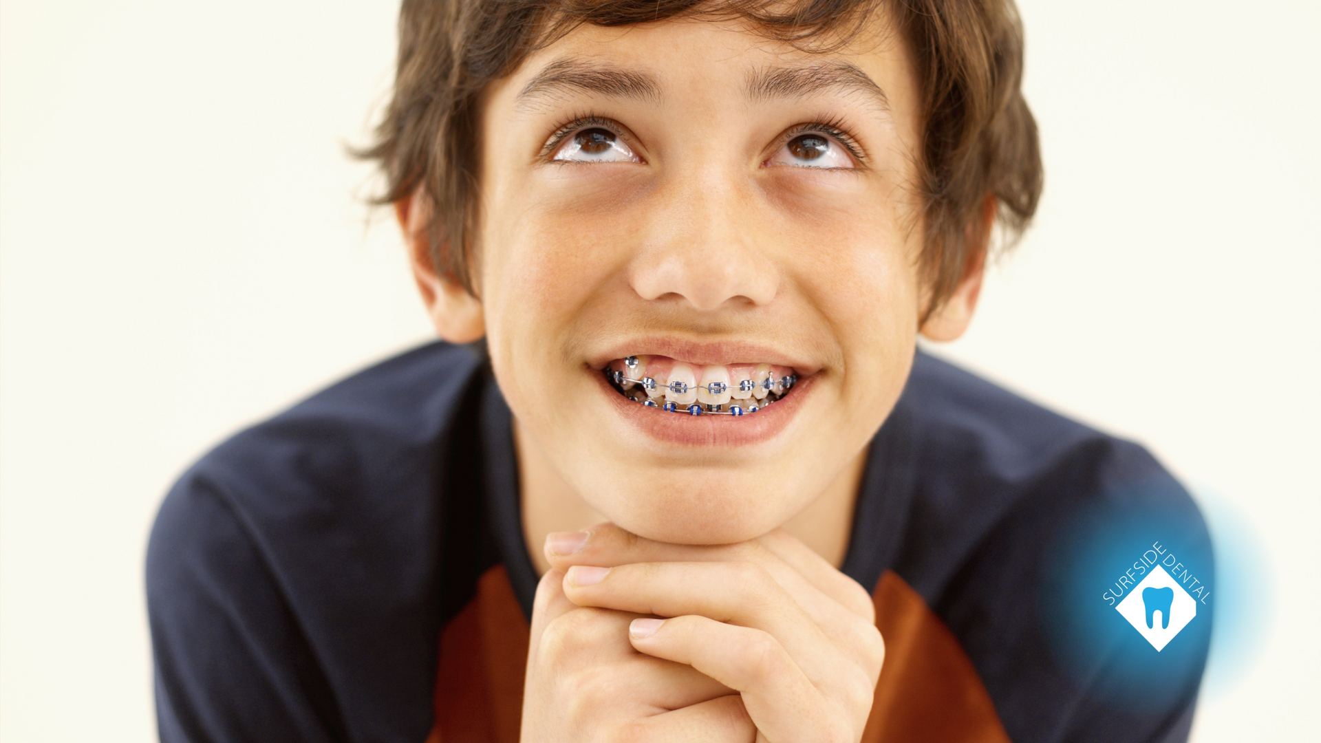 A young boy with braces on his teeth is smiling and looking up.