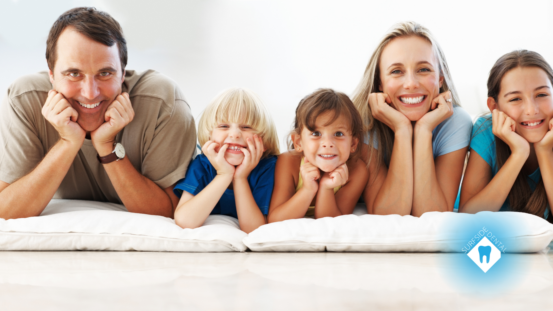 A family is laying on a bed with their hands on their chins.