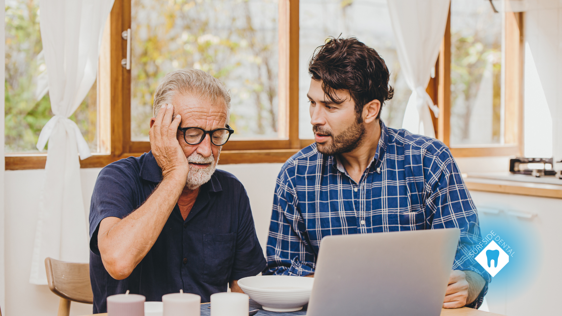 Two men are sitting at a table looking at a laptop computer.