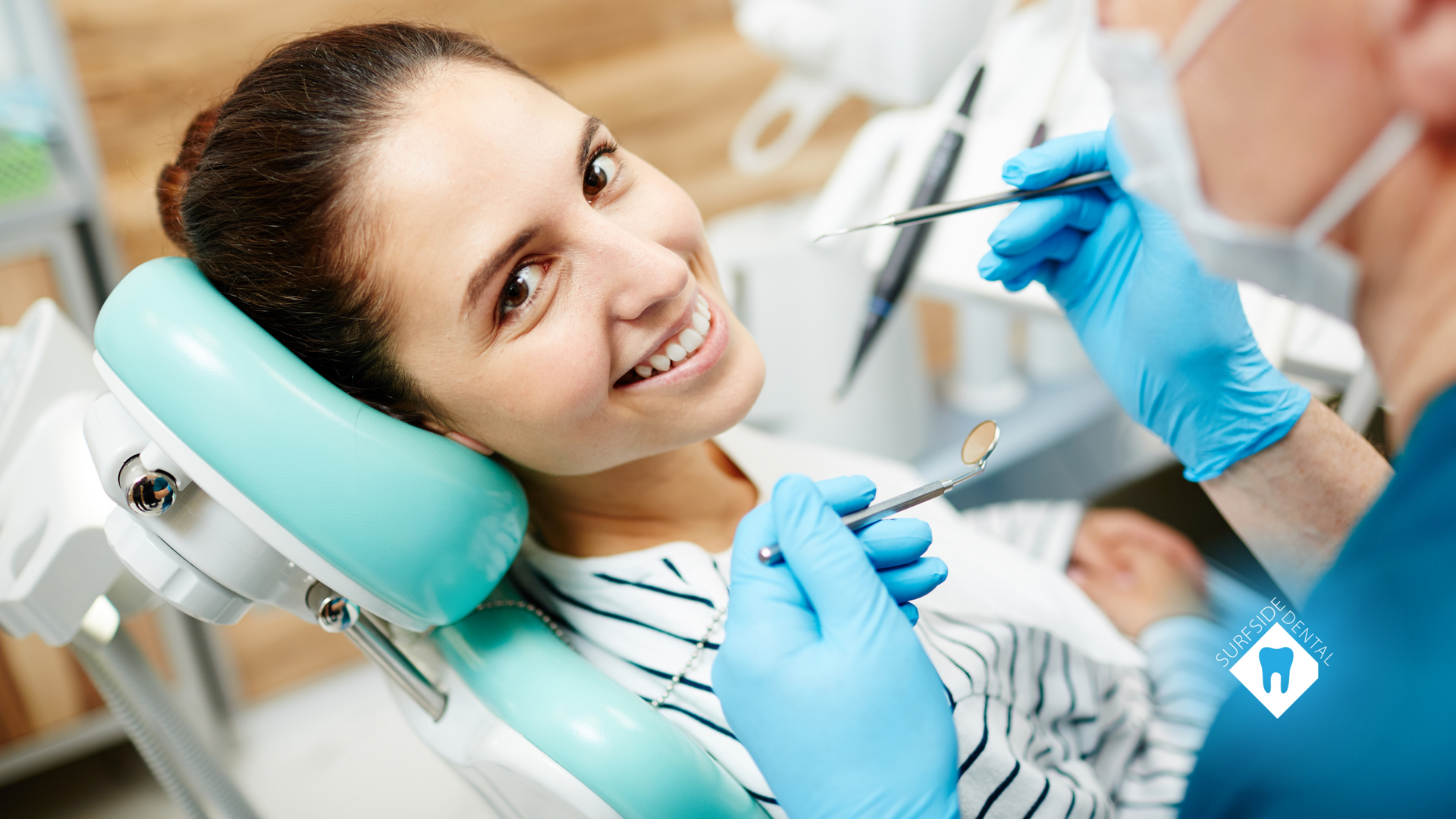 A woman is sitting in a dental chair while a dentist examines her teeth.