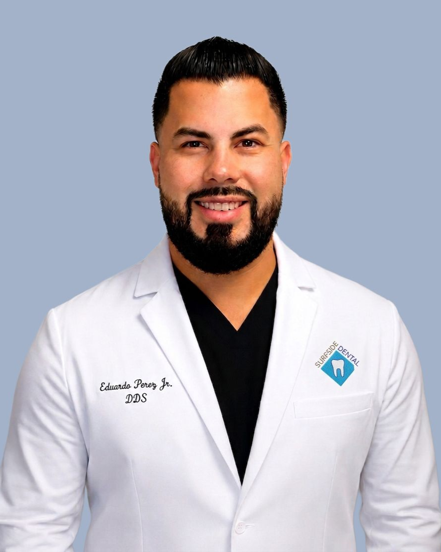 Portrait of a smiling person in a white lab coat against a light blue background.