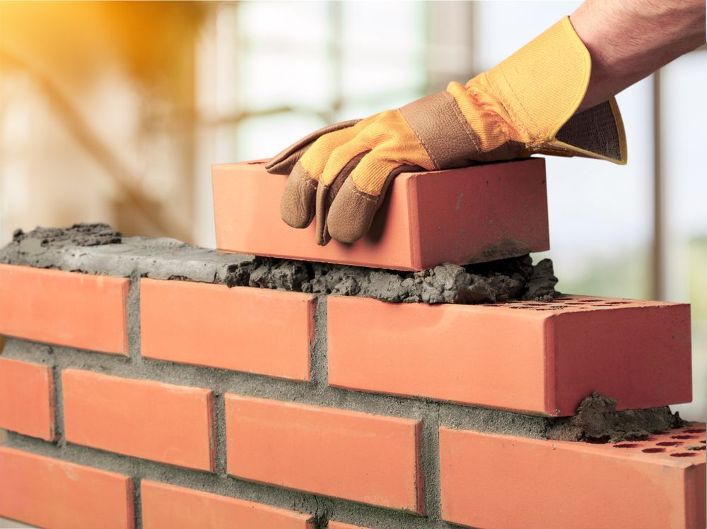 Gloved hand placing a brick on a newly built brick wall with wet mortar