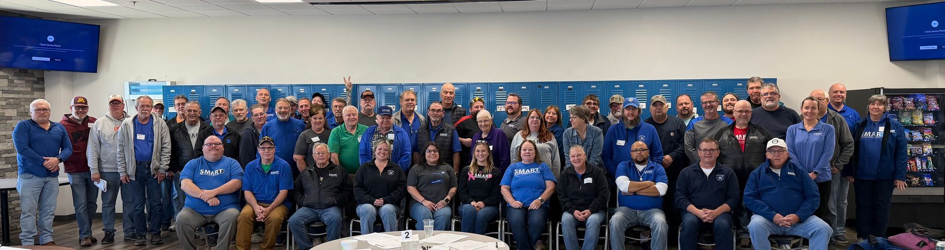 Large group posing for a team photo in a conference room, many wearing blue shirts in front of a blue backdrop.