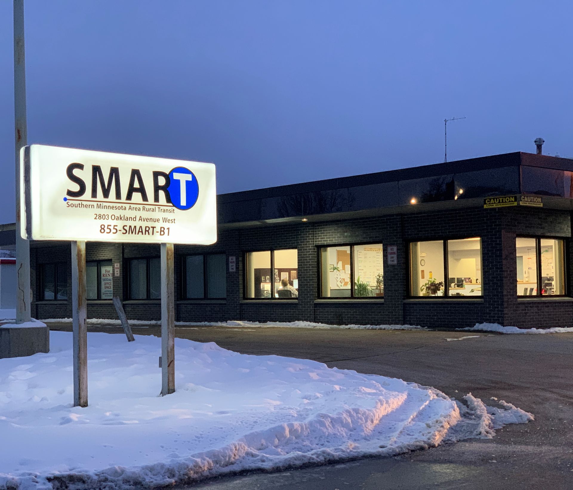 SMART sign outside a low brick building at dusk, with snow-covered ground and lit windows.