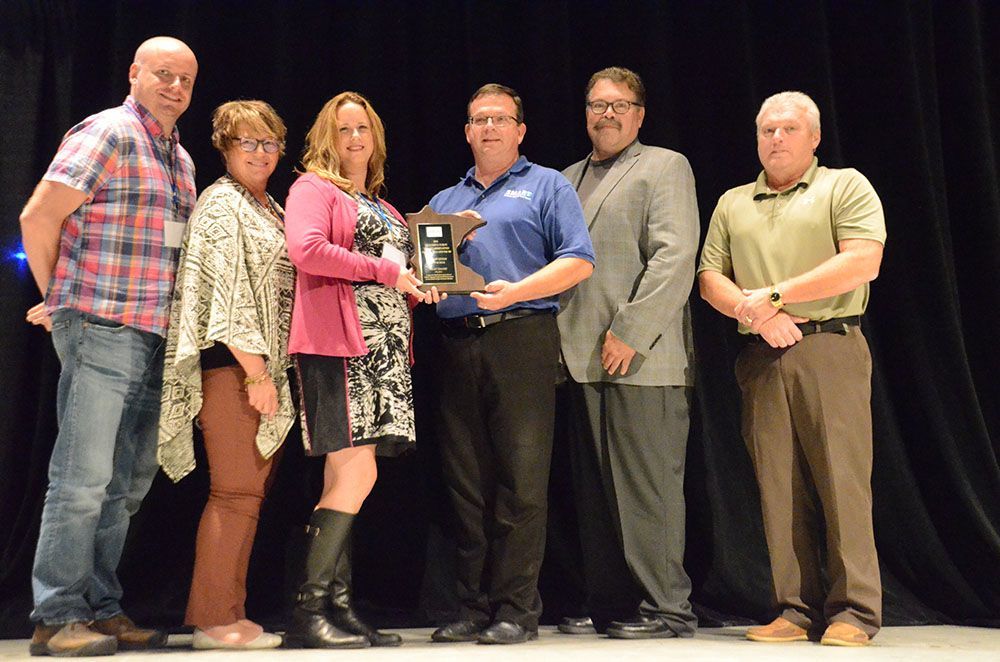 Six people on stage holding an award plaque during a presentation ceremony