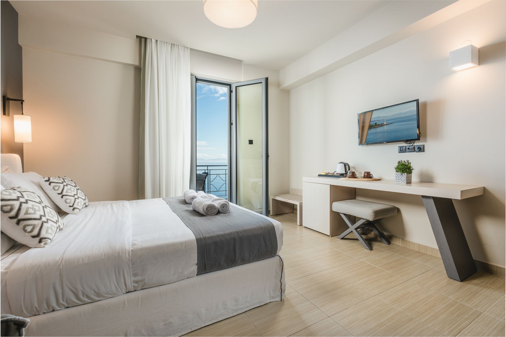 A hotel room with a bed , desk , television and balcony.