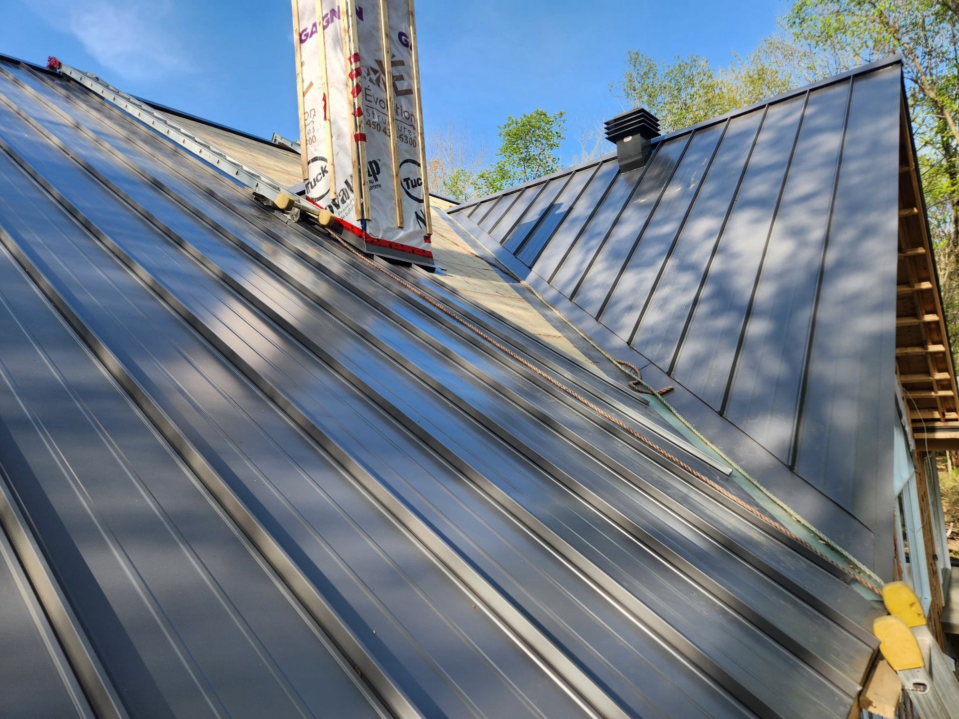 Pose d'une toiture métallique sur une maison avec cheminée et conduit de ventilation, sous un ciel bleu.