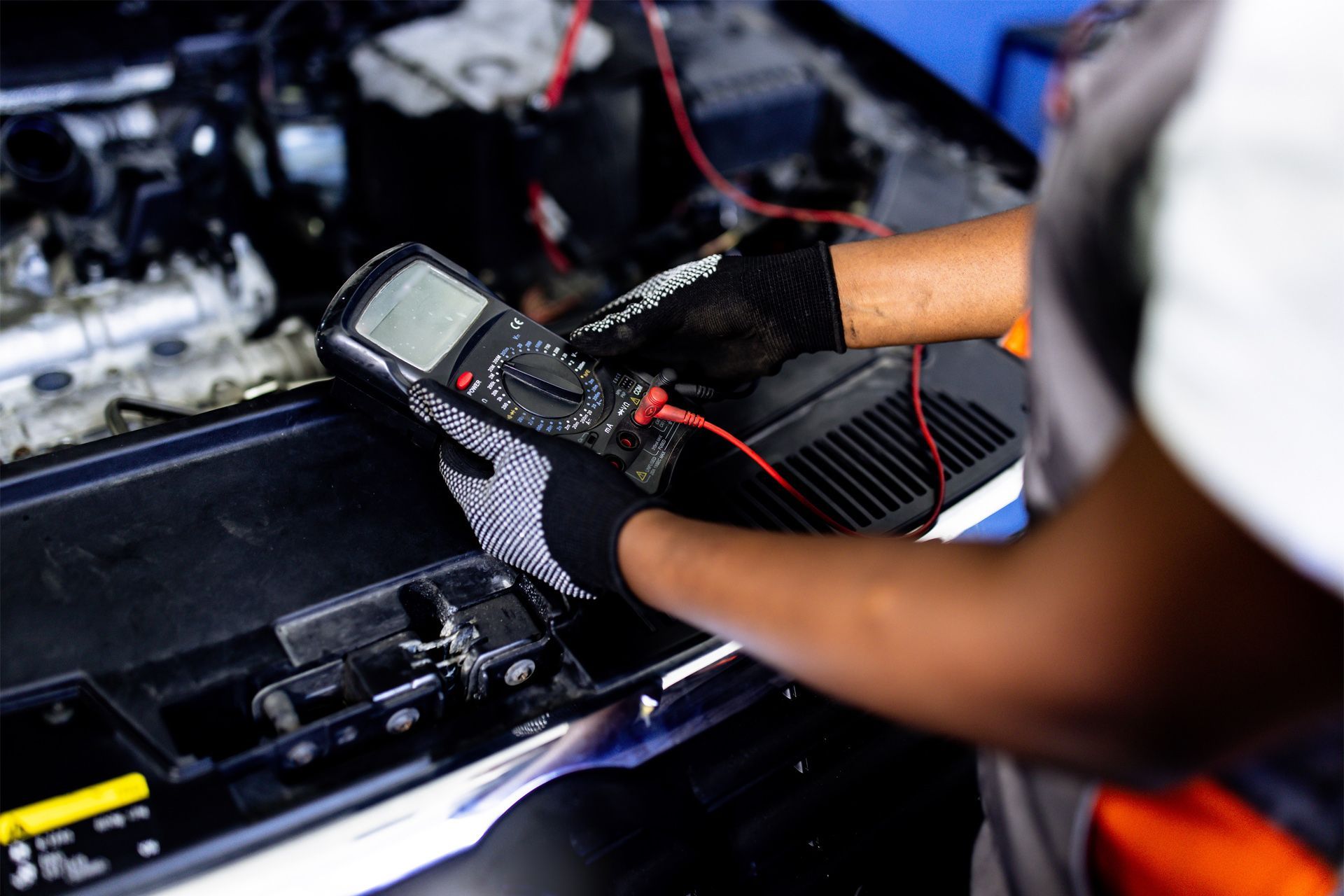 A mechanic is working on a car with a multimeter. A mechanic is working on a car with a multimeter.