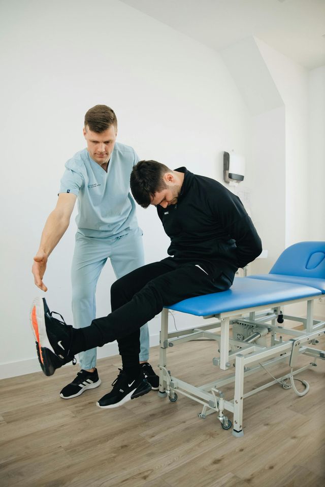 Ein Physiotherapeut unterstützt eine Person bei einer Beinhebeübung auf einer Behandlungsliege in einer Klinik.