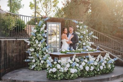 A bride and groom are standing in front of a table decorated with flowers. A bride and groom are standing in front of a table decorated with flowers.
