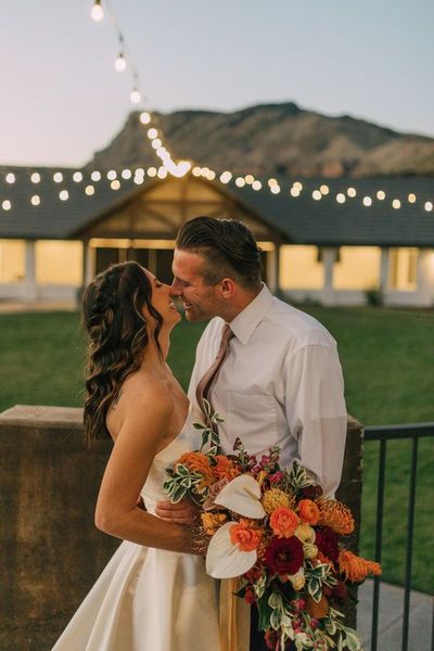 A bride and groom are kissing in front of a building while holding a bouquet of flowers. A bride and groom are kissing in front of a building while holding a bouquet of flowers.