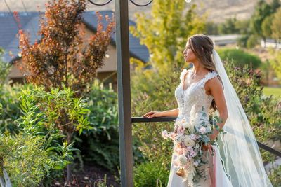 A bride in a wedding dress and veil is standing next to a railing holding a bouquet of flowers. A bride in a wedding dress and veil is standing next to a railing holding a bouquet of flowers.