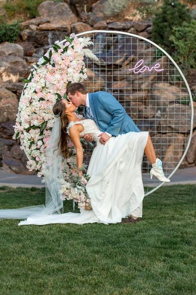 A bride and groom are kissing in front of a floral arch. A bride and groom are kissing in front of a floral arch.