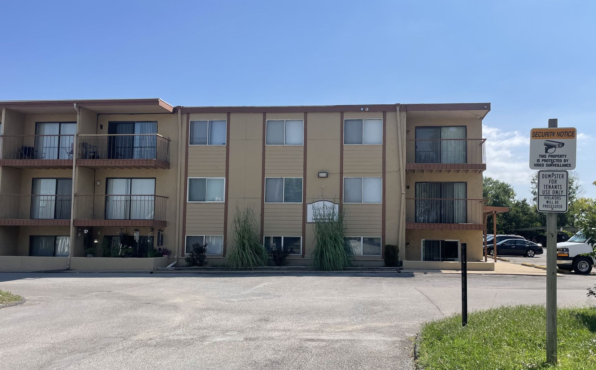 Tan apartment building with balconies, parking lot, and parking restriction sign.