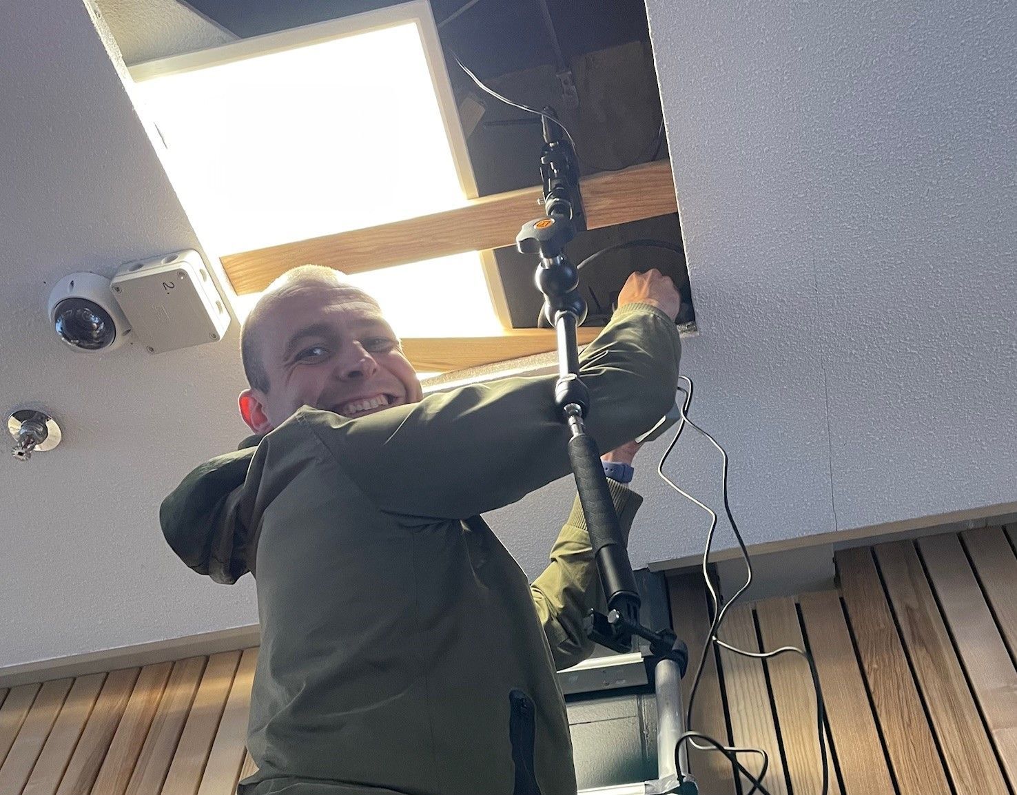 A man in a green jacket is working on a camera on a tripod.