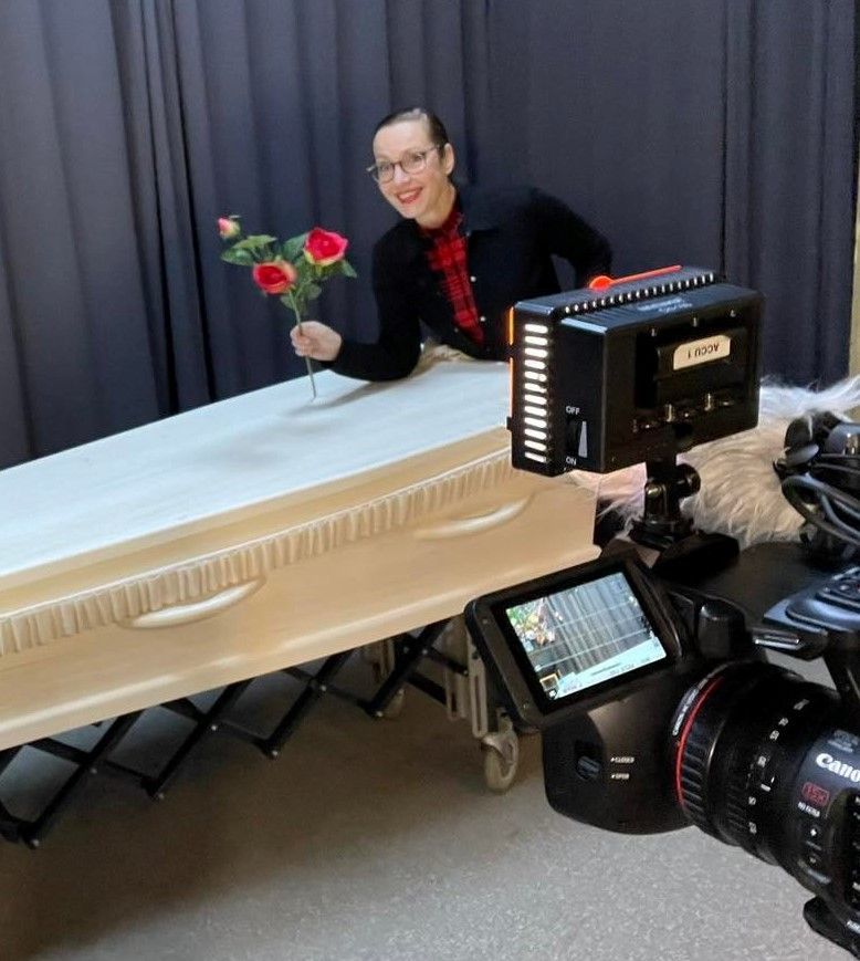 Persoon met rozen naast een doodskist, poserend voor de camera. Studio met grijze achtergrond.