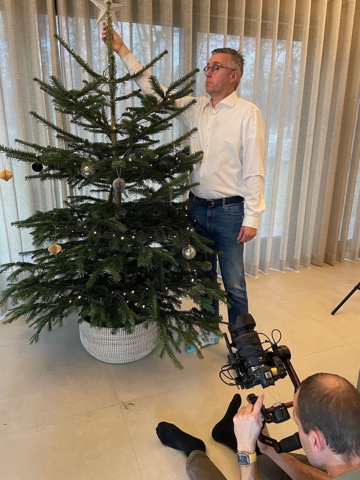 Een man versiert een kerstboom in de woonkamer.