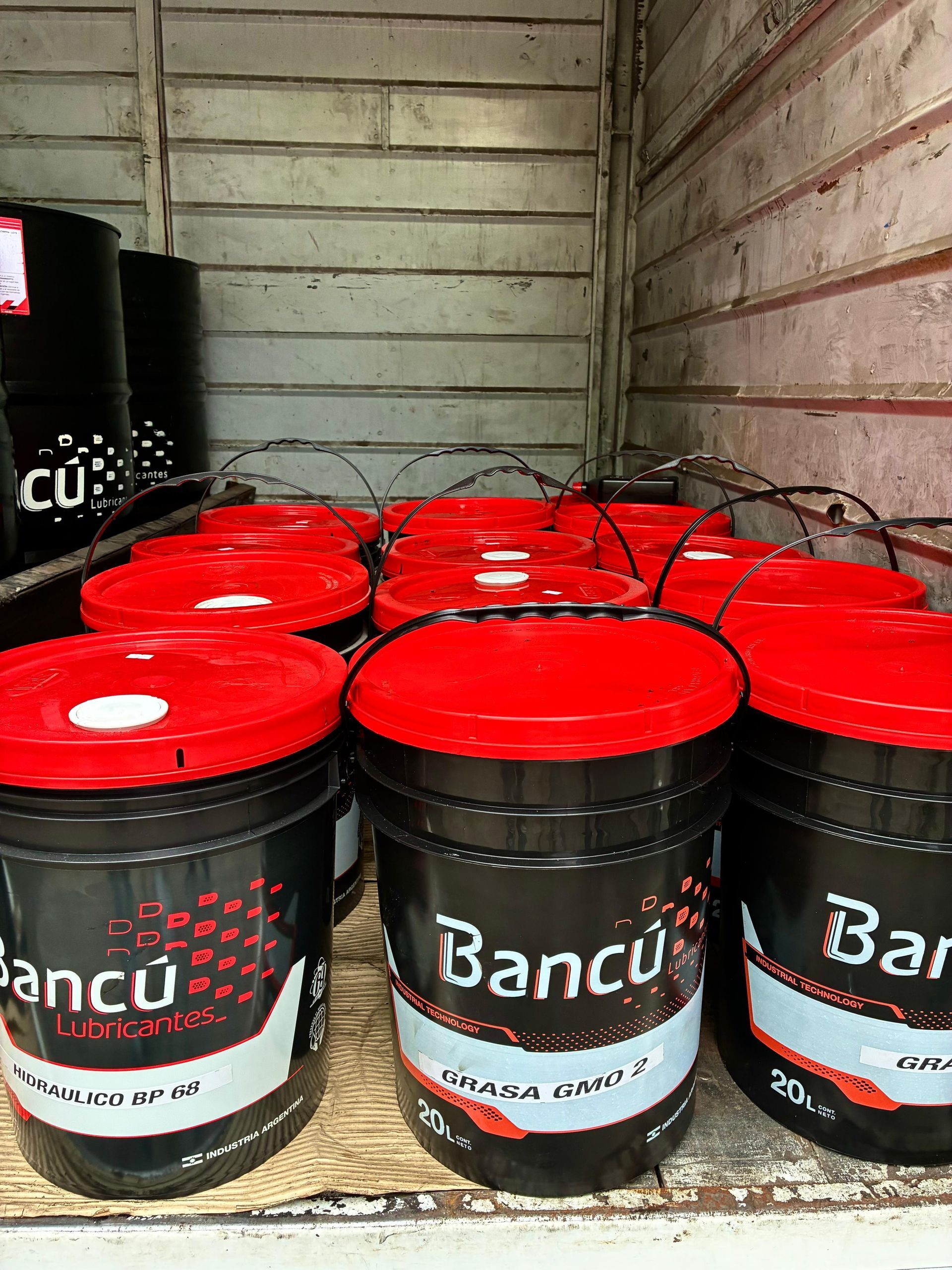 Cubos de pintura negros y rojos con asas apilados en un camión, etiquetados