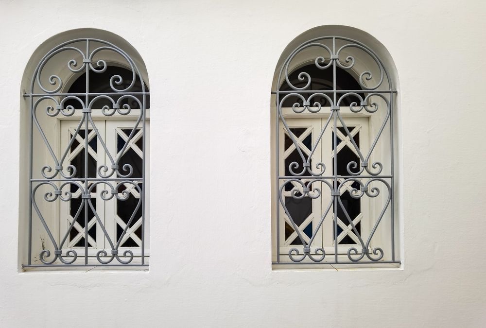 Due finestre ad arco con sbarre in ferro battuto su un muro bianco