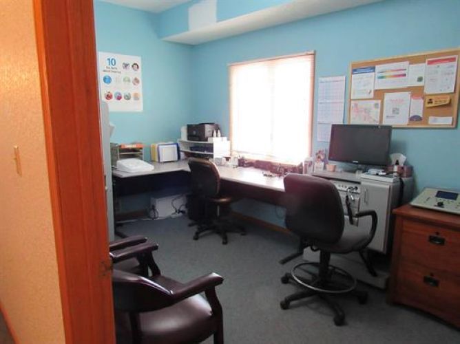 Small office with desks, computer monitors, chairs, and a bulletin board in a blue-walled room.