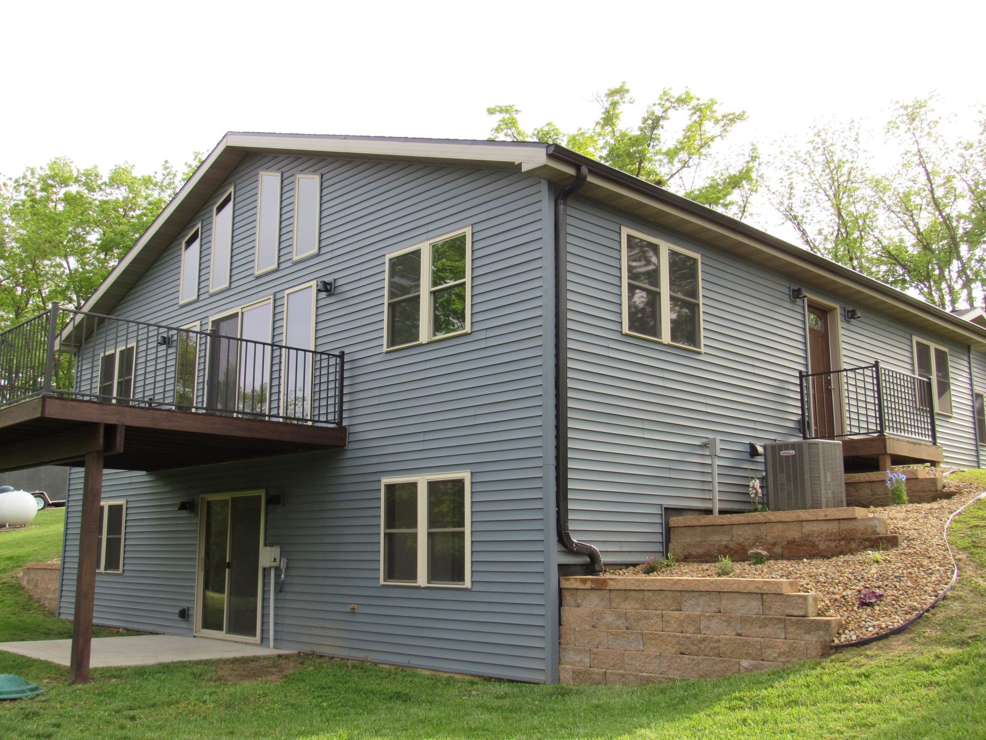 Blue two-story house with deck and stone retaining wall on a grassy hillside