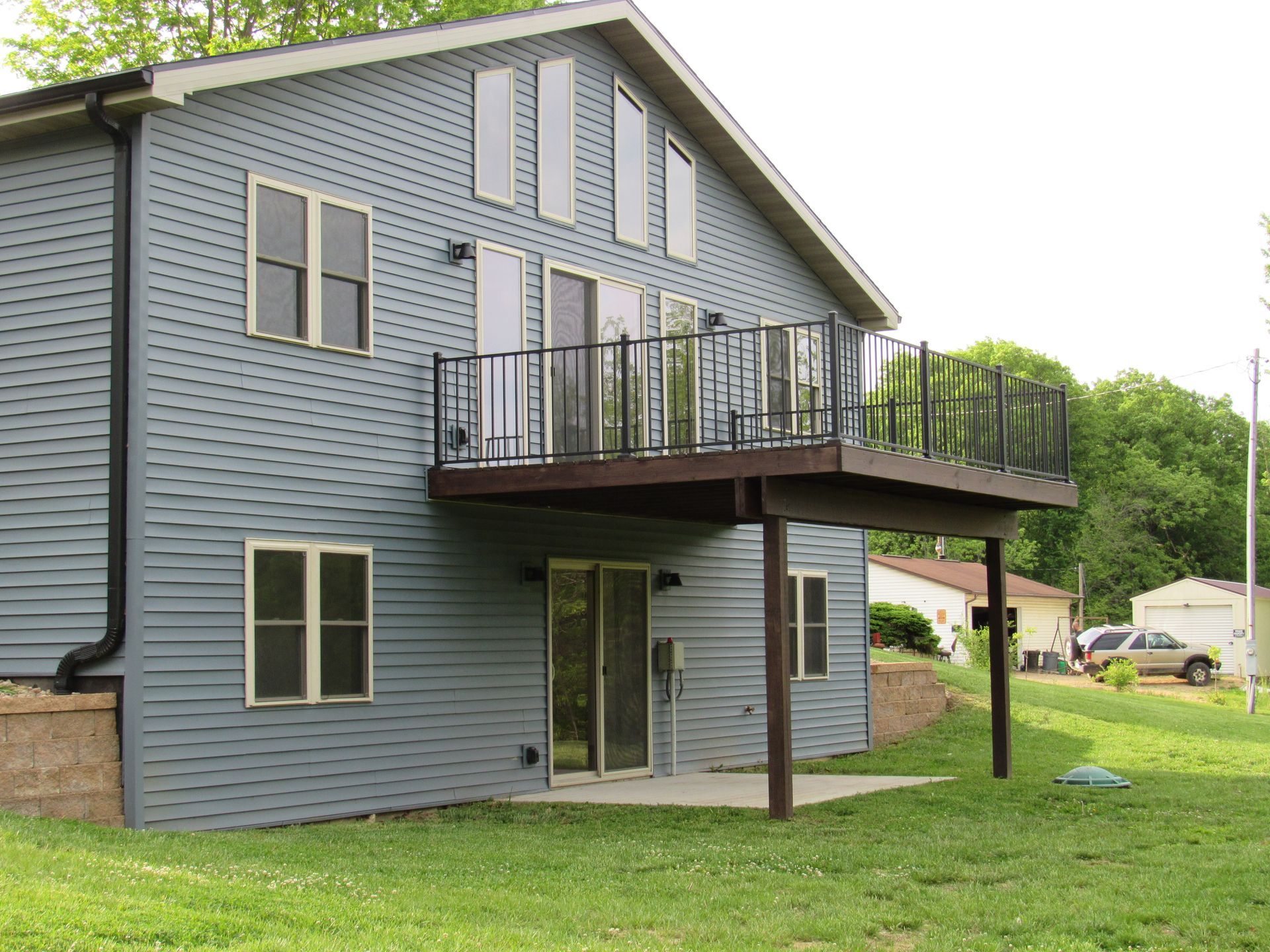 Two-story blue house with a raised deck and black railings on a grassy lot