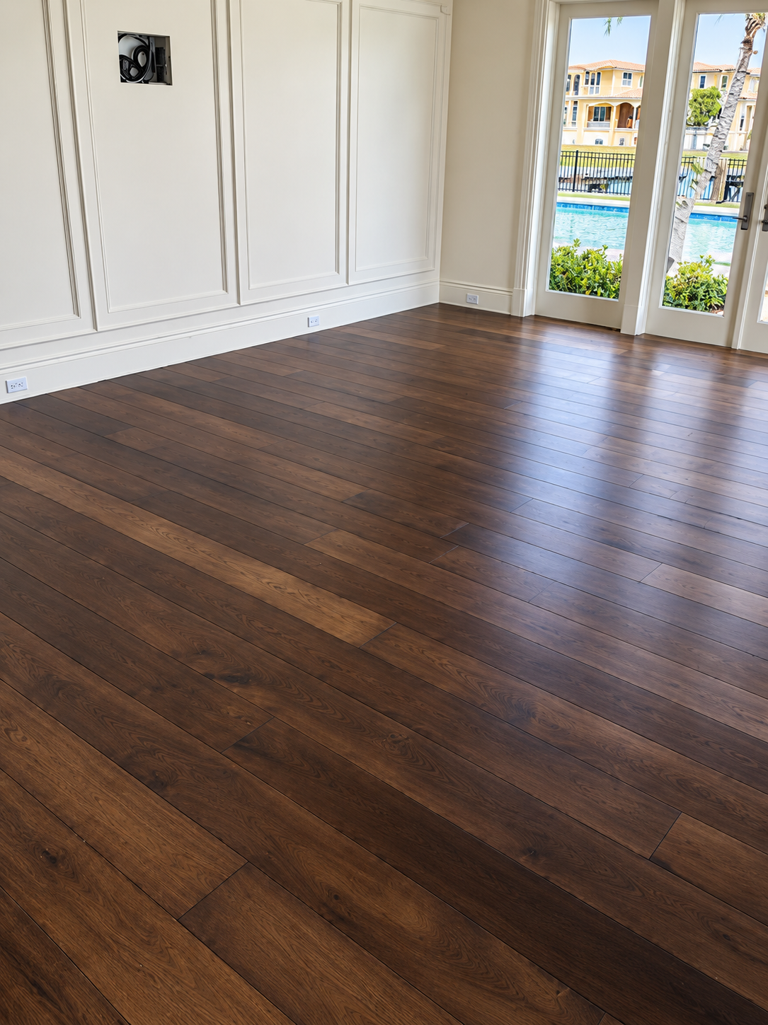Empty room with dark wood floors and white walls, opening to a bright balcony view