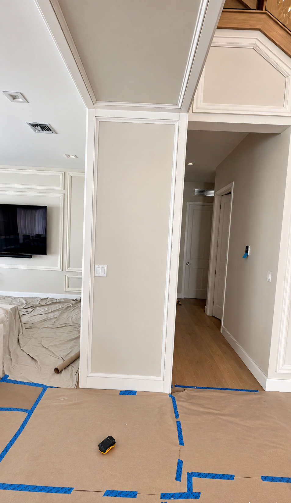 Interior hallway and room under renovation, with taped-off floor and fresh beige walls.
