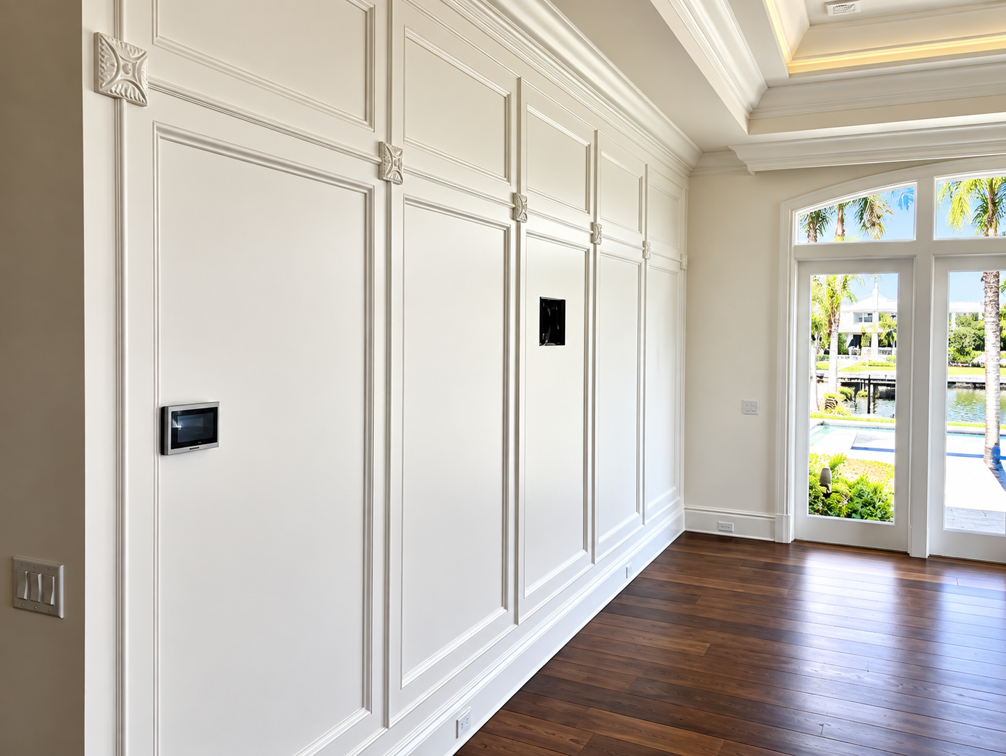 Bright foyer with white paneled walls, dark wood floor, and glass doors opening outside.