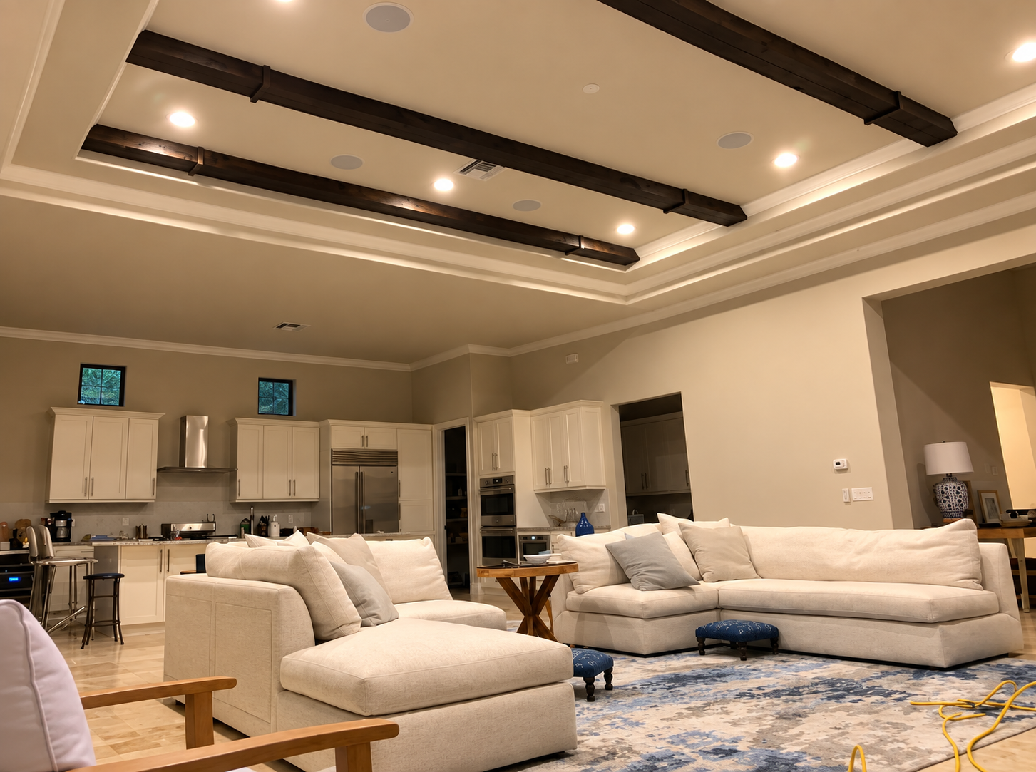 Bright modern living room with white sofas, blue rug, recessed ceiling lights, and kitchen in background