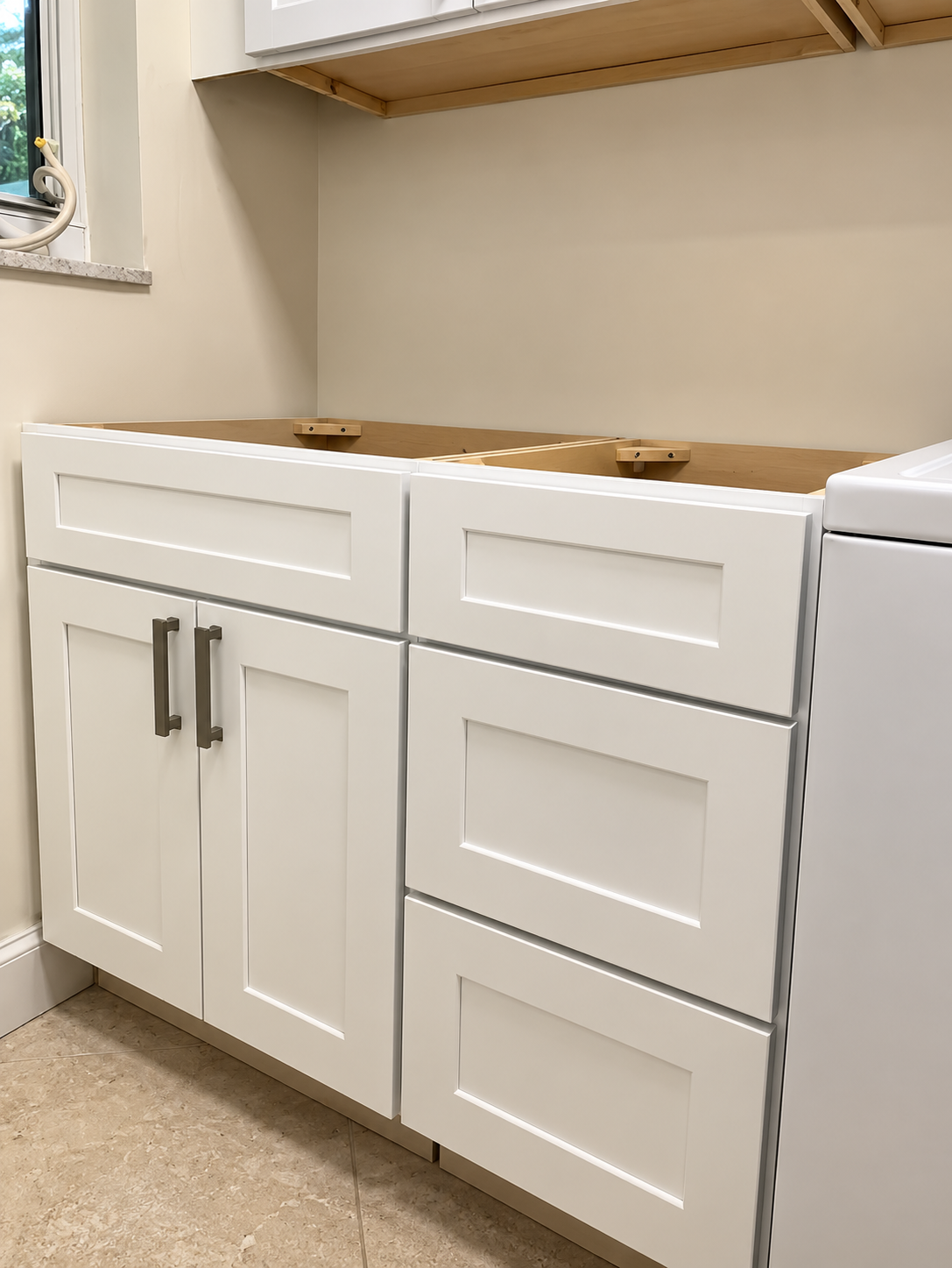 White bathroom vanity with drawers and cabinet beneath a beige countertop, under a wall cabinet.