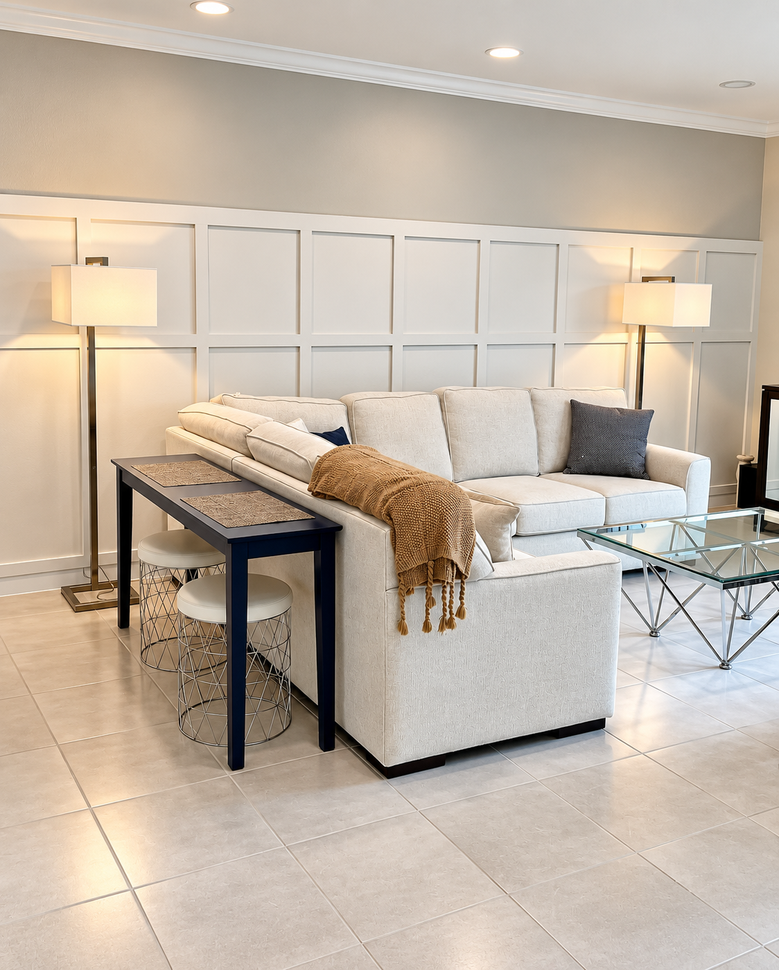 Bright living room with white sofa, floor lamps, paneled wall, and navy side table on tile floor