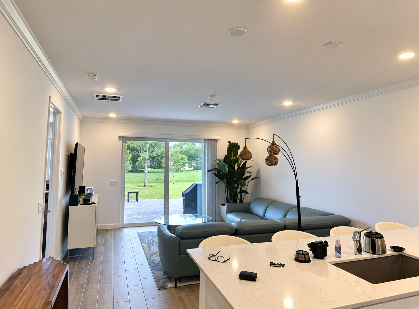 Bright modern living room with white walls, gray sofa, kitchen island, and sliding doors to a green yard