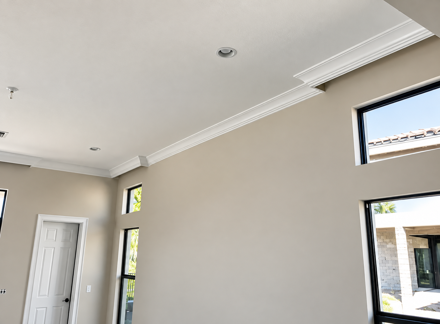Empty modern room with beige walls, white trim, and tall windows letting in daylight