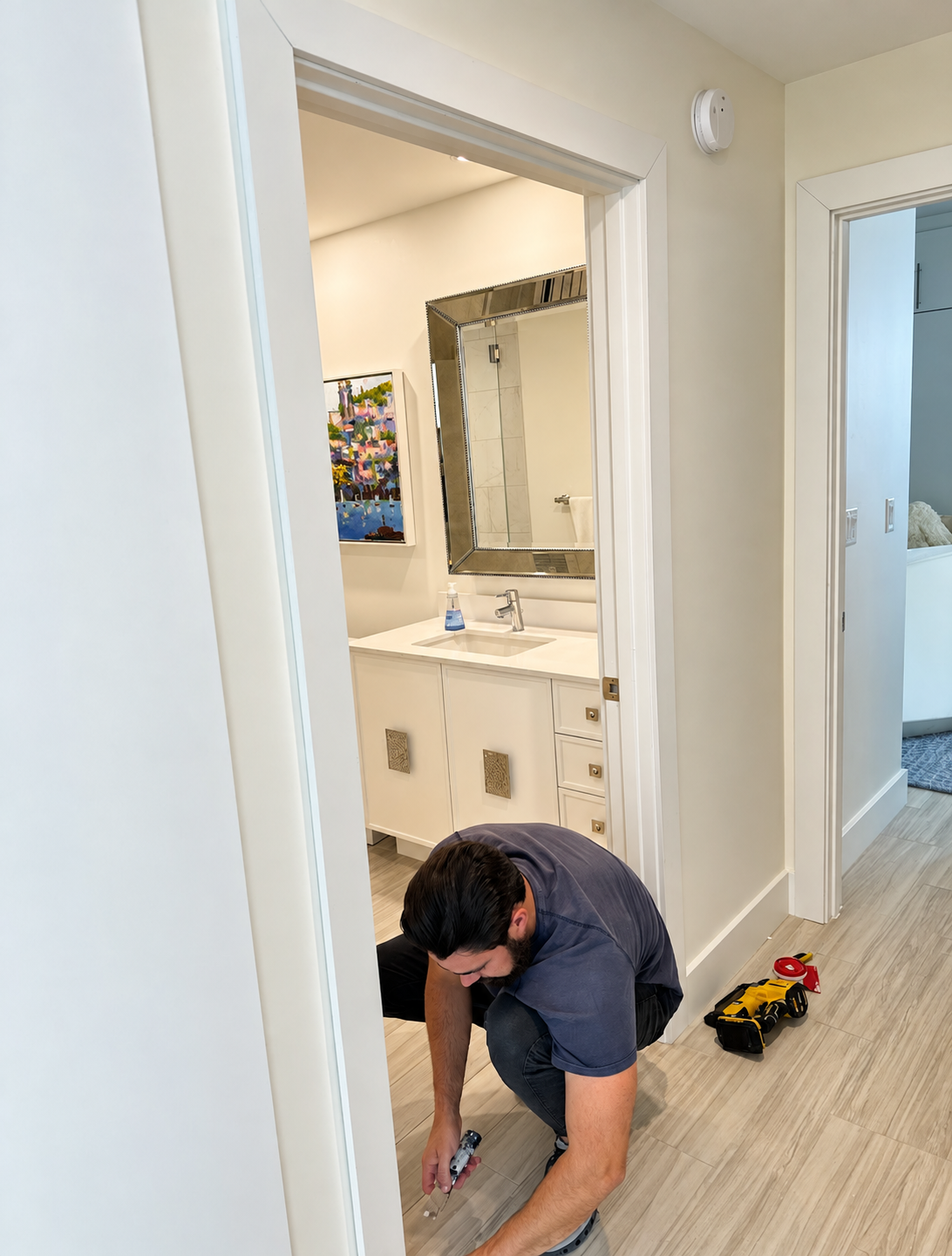 Worker crouched in a hallway measuring flooring beside a bathroom and toy truck
